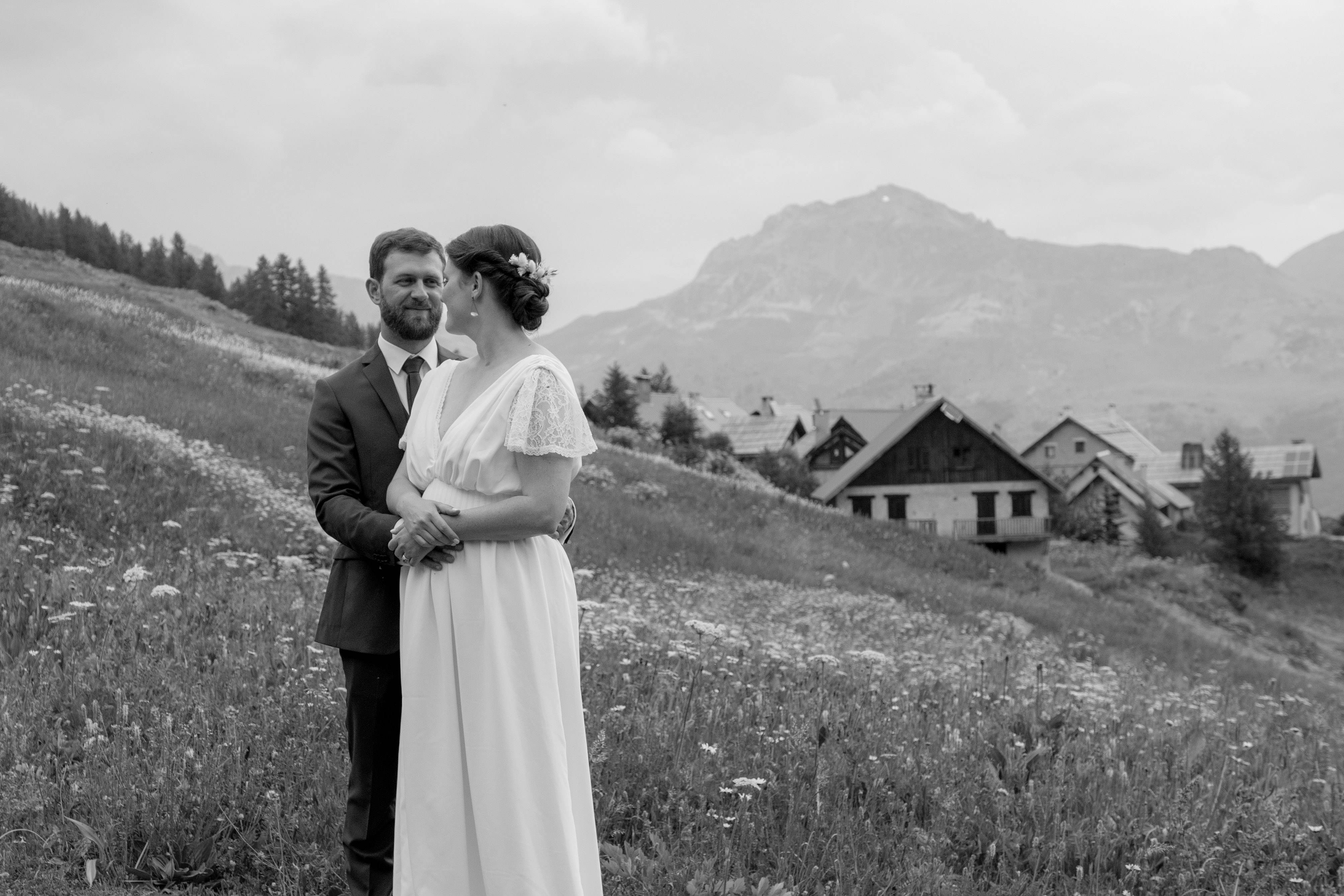 Mariés dans un pré, hameau de montagne en arrière-plan, noir et blanc