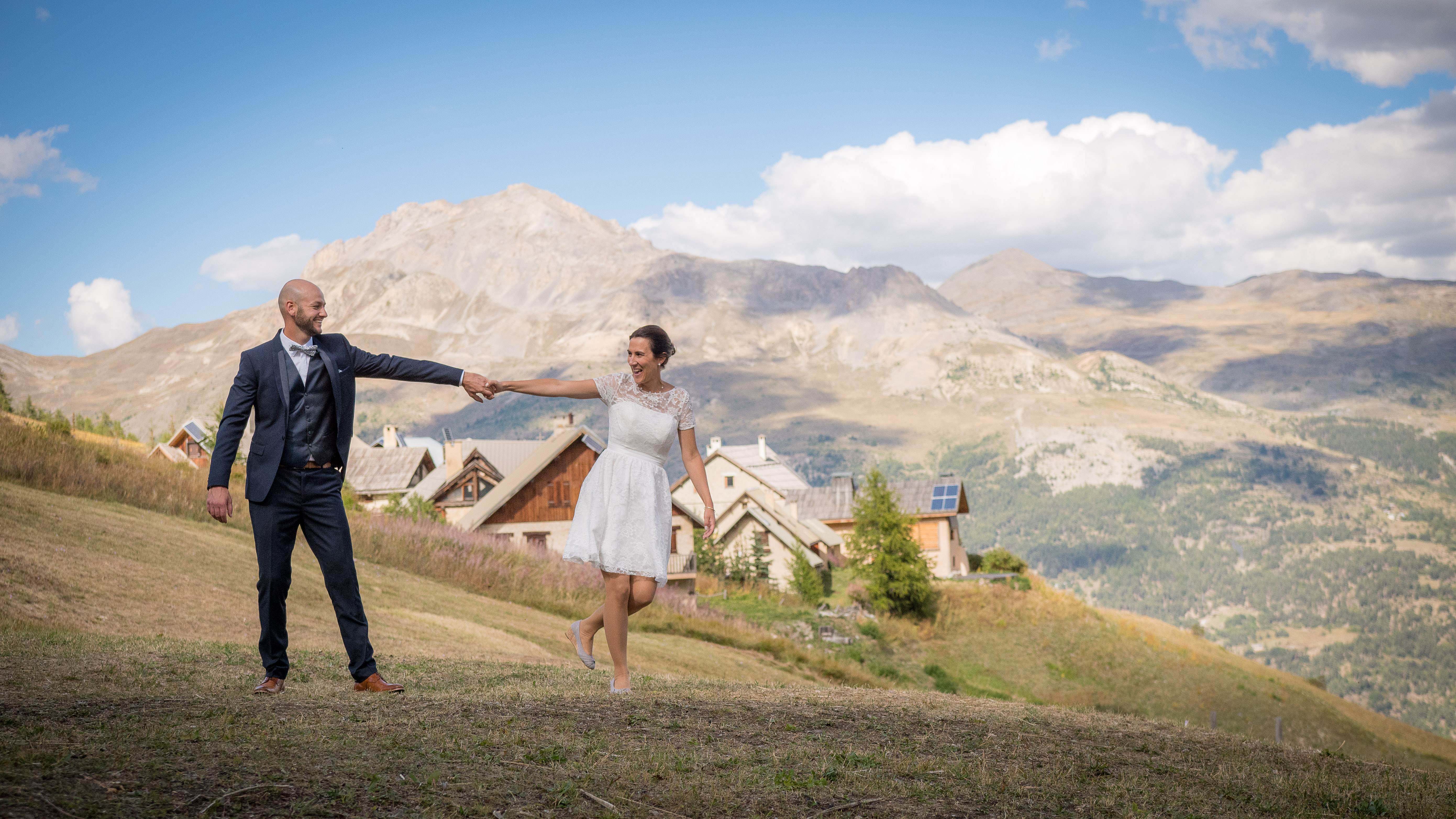 Couple de mariés dans un alpage, chalets et sommets en arrière-plan