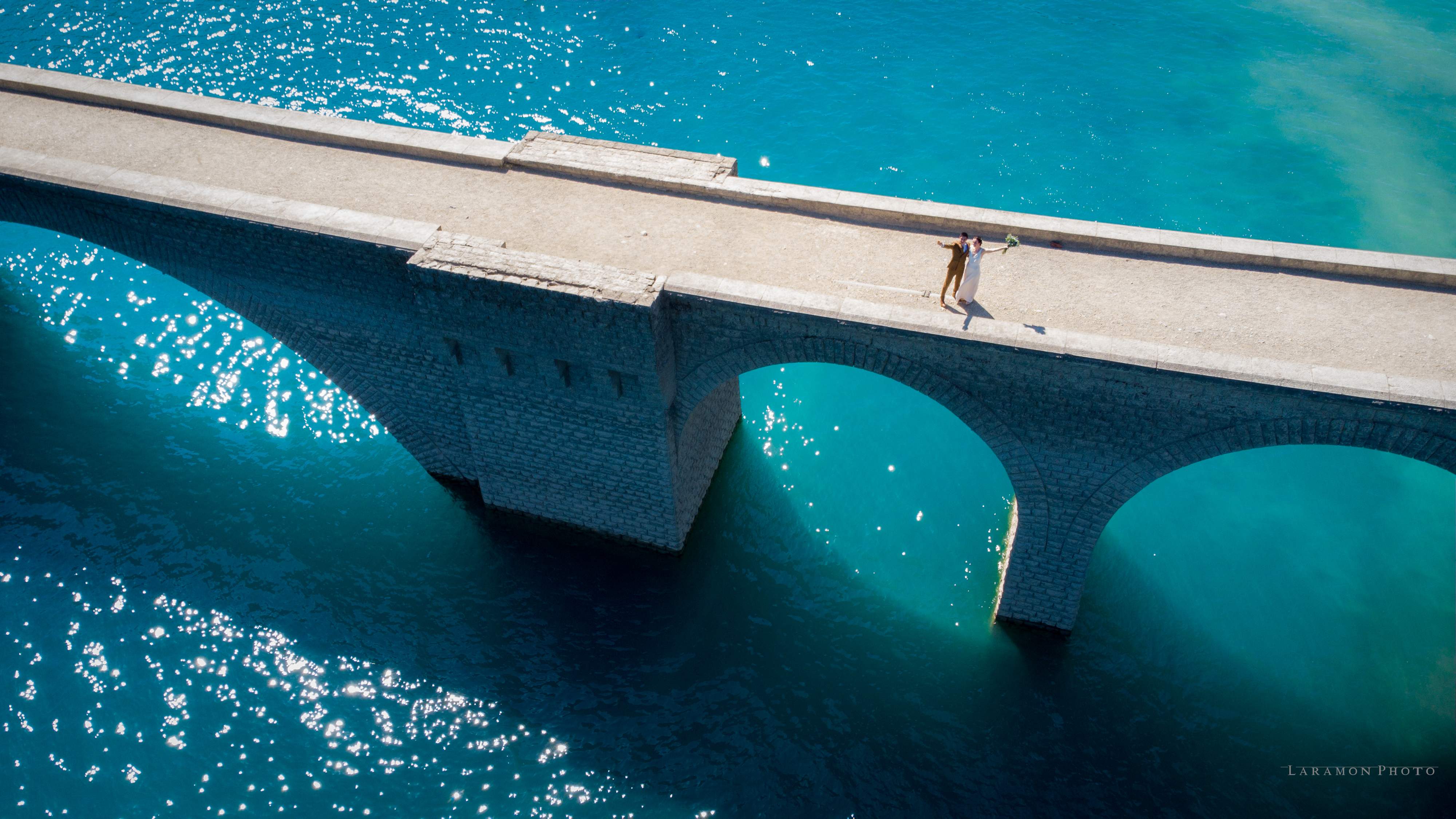 Aerial drone view — couple on a bridge above turquoise lake