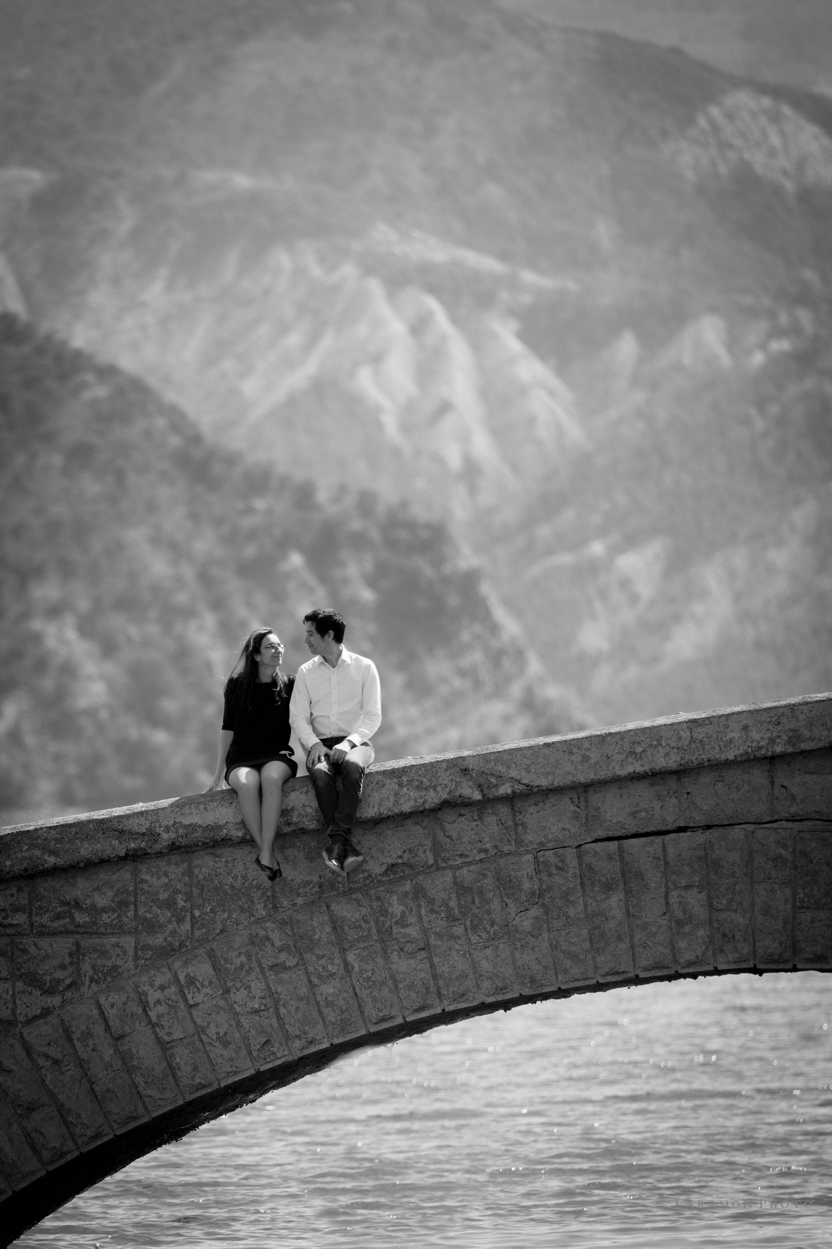 Couple assis sur un pont de pierre au pied d’une paroi rocheuse